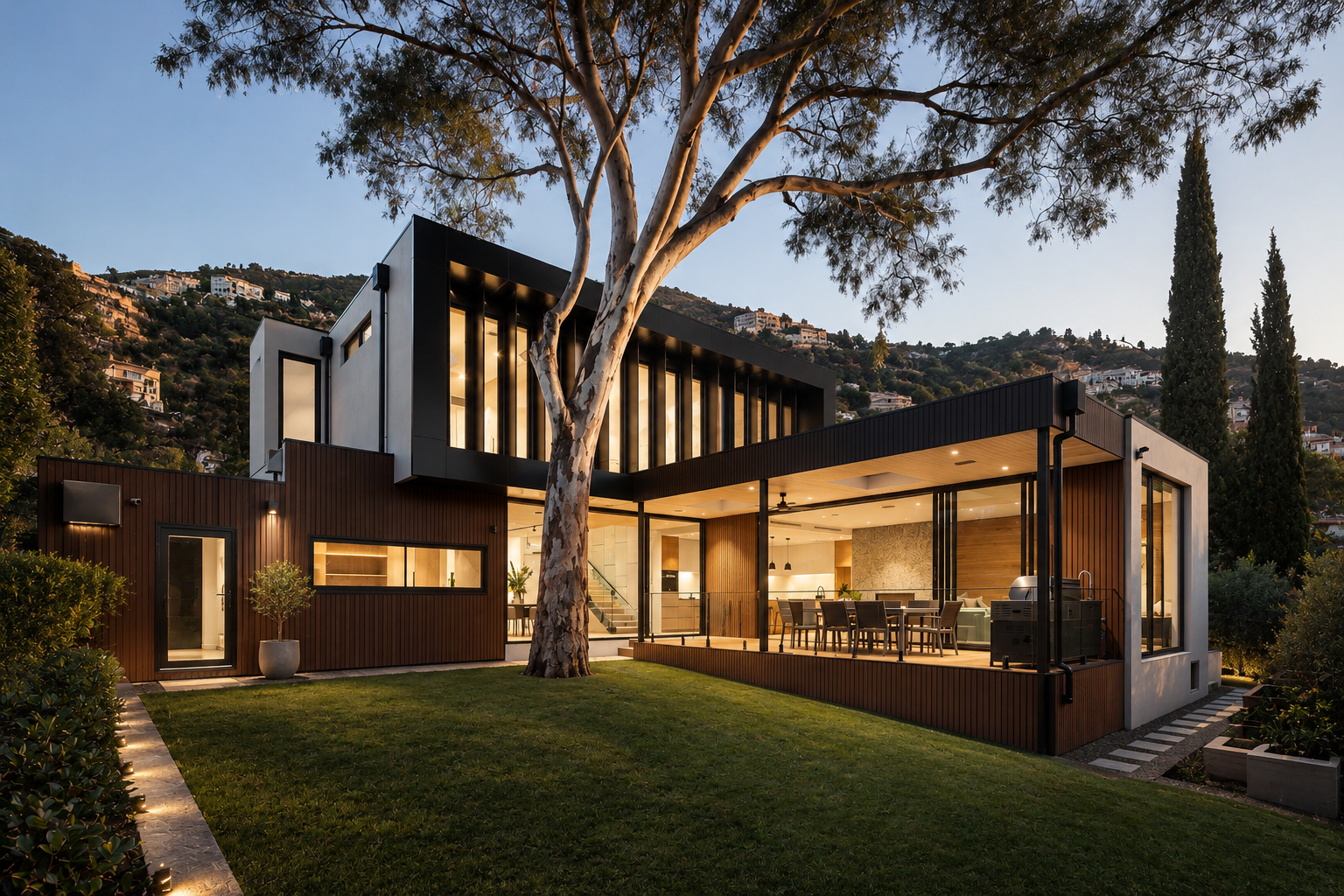 Dark house glowing at dusk beneath a large tree and green lawn
