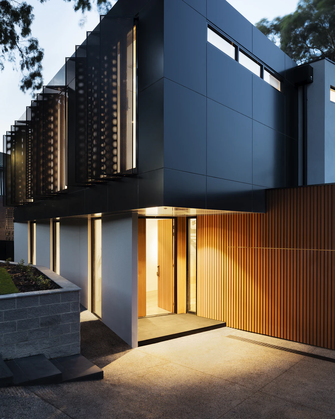 Warmly lit entry between a dark volume and a timber wall